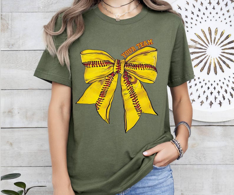 May include: A green t-shirt featuring a yellow softball bow and the text "Your Team" printed on the front.
