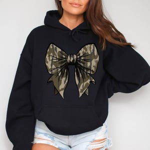 May include: Black hooded sweatshirt with a large camouflage bow design on the front.
