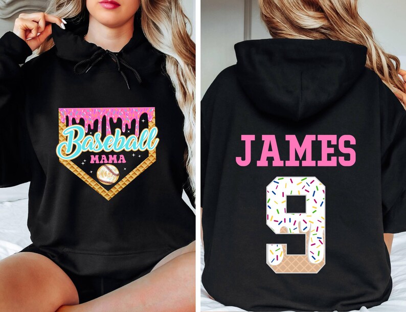 K&ouml;nnte beinhalten: Schwarzer Kapuzenpullover mit einem pinkfarbenen und blauen Baseball-Motiv auf der Vorderseite, auf dem "Baseball Mama" steht, und einer pinkfarbenen und wei&szlig;en Eiswaffel-Nummer 9 auf der R&uuml;ckseite mit dem Namen "JAMES" dar&uuml;ber.