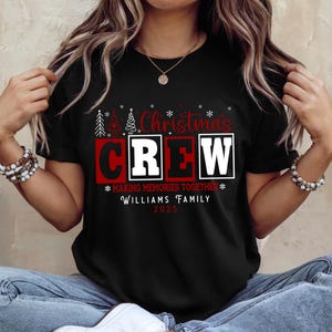 May include: Black t-shirt with the words "Christmas CREW" in white and red block letters. The shirt also includes the text "MAKING MEMORIES TOGETHER" and "WILLIAMS FAMILY 2023" in white. Festive Christmas tree graphics are above the word "Christmas".