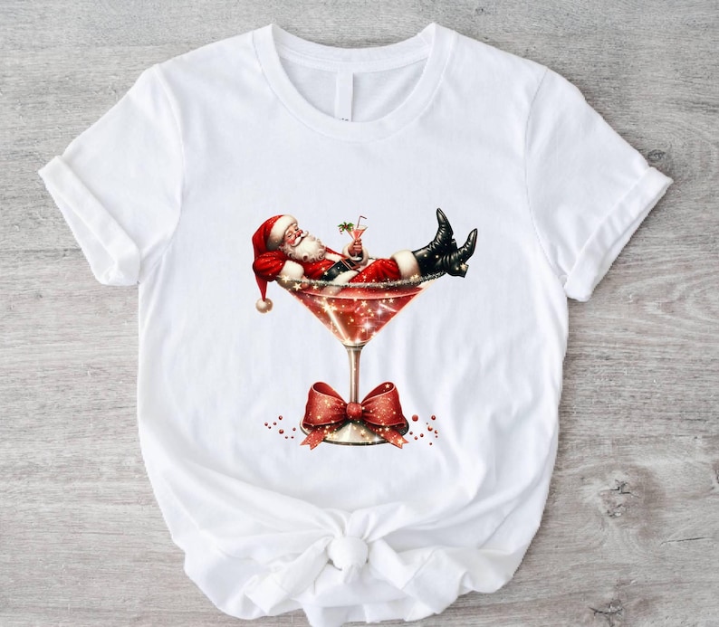 May include: White t-shirt with a graphic of Santa Claus relaxing in a martini glass with a red bow on the stem.