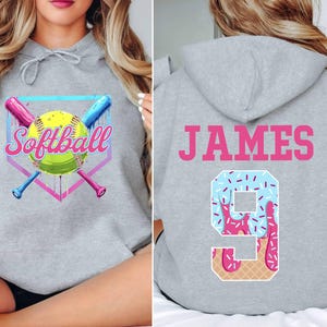 May include: Gray hooded sweatshirt with a softball graphic on the front and the name "JAMES" and a number "9" with a pink and blue ice cream design on the back.