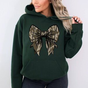 May include: A dark green hooded sweatshirt with a large camouflage bow design on the front.