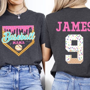 May include: Two gray t-shirts with a baseball theme. One shirt has a pink and white baseball diamond with the text "Baseball Mama" and a baseball graphic. The other shirt has the text "JAMES" and the number "9" with a pink and white ice cream cone graphic.