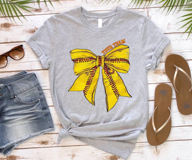 May include: Grey t-shirt with a yellow softball bow and the text "Your Team" printed on the front.