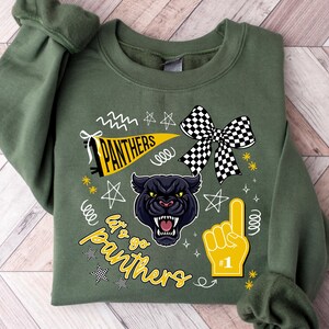 May include: Olive green sweatshirt with a graphic design featuring a black panther, a yellow pennant with "PANTHERS" text, a checkered bow, and a foam finger. The text "Let's go Panthers" is also included.