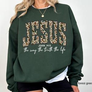 May include: Forest green sweatshirt with the word "JESUS" in a camouflage pattern. Below the word "JESUS" is the text "JOHN 14:6" and the phrase "the way the truth the life" in a script font.