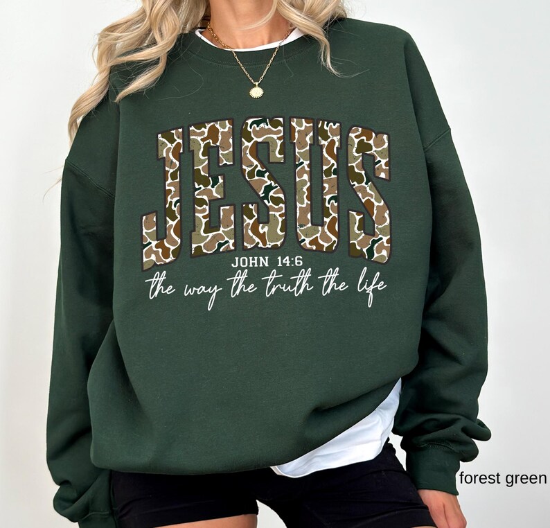 May include: Forest green sweatshirt with the word "JESUS" in a camouflage pattern. Below the word "JESUS" is the text "JOHN 14:6" and the phrase "the way the truth the life" in a script font.