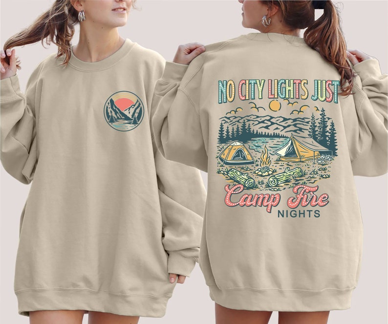 May include: A beige sweatshirt with a graphic of a mountain scene and the text "No City Lights Just Camp Fire Nights" on the back. The front of the sweatshirt has a smaller graphic of a mountain scene.