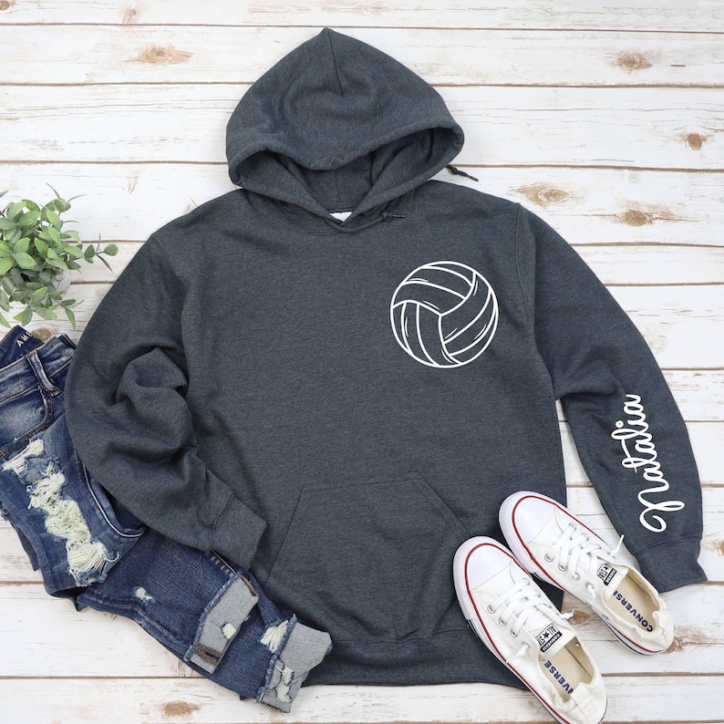 May include: A dark gray hooded sweatshirt with a white volleyball graphic on the front and the name "Natalia" written on the sleeve.