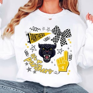 May include: White sweatshirt with a black panther graphic, a checkered bow, and the text "Let's Go Panthers." The design includes stars, a foam finger, and a pennant. The sweatshirt is a fan item.