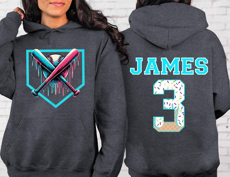 May include: Dark gray hoodie with a baseball-themed graphic on the front, featuring crossed bats and a baseball within a teal outline. The back displays the name "JAMES" and the number "3" with a sprinkle-covered design.