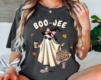 May include: A dark gray t-shirt with a graphic of a ghost wearing a witch hat and sunglasses, holding a coffee cup and a leopard print purse. The text "BOO-JEE" is printed on the shirt.
