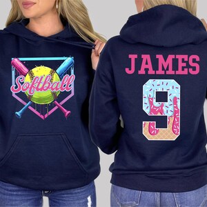 May include: Two navy blue hooded sweatshirts. One sweatshirt has a graphic of a softball with crossed bats and the text "Softball". The other sweatshirt has the text "JAMES" and the number "9" with a pink and blue ice cream cone design.
