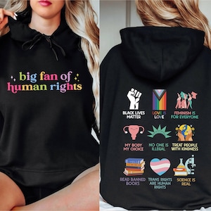 May include: Black hoodie with the text "big fan of human rights" in rainbow colors on the front. The back features various graphics and phrases, including "Black Lives Matter," "Love is Love," and "Feminism is for Everyone."