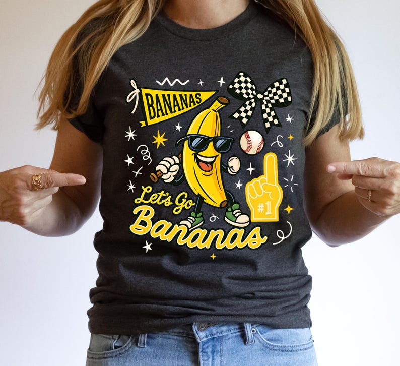 May include: Dark gray t-shirt with a cartoon banana wearing sunglasses and sneakers. The shirt features the text "BANANAS" on a banner and "Let's Go Bananas" in yellow script, along with baseball and foam finger graphics.