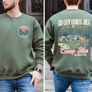 May include: A green sweatshirt with a graphic of a mountain scene and the text "No city lights just camp fire nights" on the back. The front of the sweatshirt has a smaller graphic of a mountain scene.