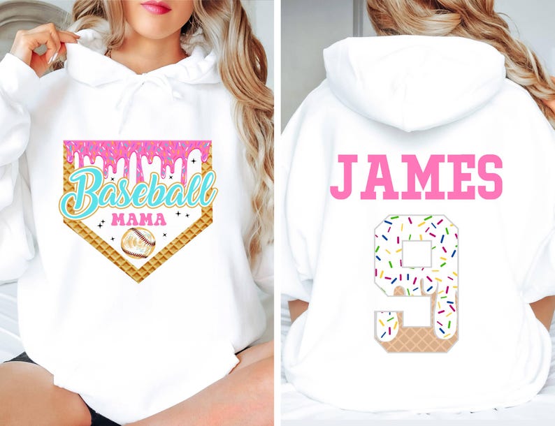 K&ouml;nnte beinhalten: Wei&szlig;er Hoodie mit einem rosa und blauen Baseball-Motiv auf der Vorderseite, auf dem "Baseball Mama" steht, und einer pinkfarbenen Nummer 9 mit Streuseln auf der R&uuml;ckseite, auf der "JAMES" steht.