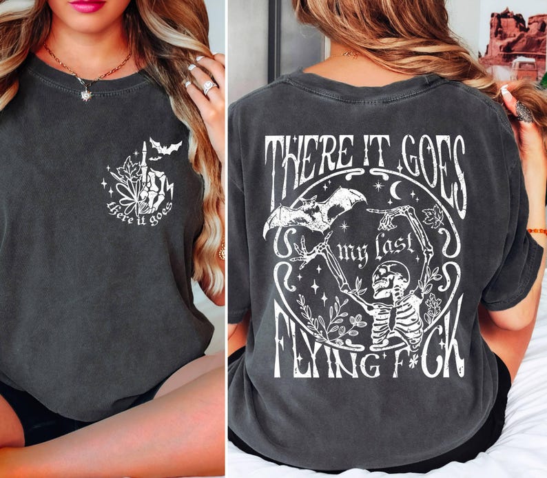 K&ouml;nnte beinhalten: Ein dunkelgraues T-Shirt mit einem wei&szlig;en Grafikdruck eines Skeletts, das eine Fledermaus h&auml;lt, und dem Text "There it goes my last flying f*ck".