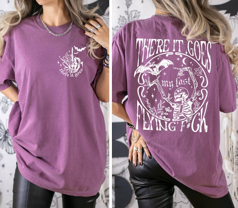 K&ouml;nnte beinhalten: Ein lilafarbenes Oversize-T-Shirt mit einem wei&szlig;en Grafikdruck eines Skeletts, das eine Fledermaus mit dem Text "There it goes my last flying f*ck" h&auml;lt.