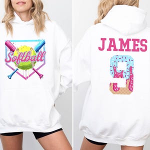 May include: White hooded sweatshirt with a pink and blue softball graphic on the front and the text "JAMES 9" on the back. The number 9 is decorated with a pink and blue ice cream cone design.