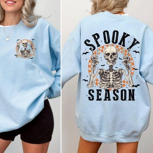 Puede incluir: Sudadera azul claro con un gr&aacute;fico de esqueleto y el texto "Spooky Season" impreso en la parte delantera.