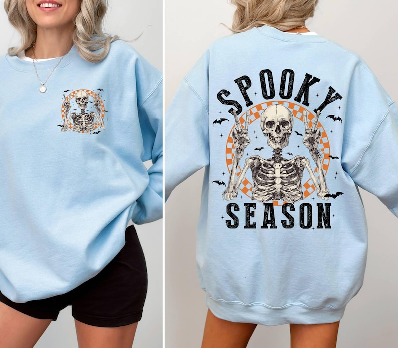 Puede incluir: Sudadera azul claro con un gr&aacute;fico de esqueleto y el texto "Spooky Season" impreso en la parte delantera.