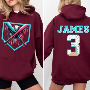 May include: Burgundy hoodie with a baseball-themed graphic on the front, featuring crossed bats and a baseball within a home plate outline. The back displays the name "JAMES" and the number "3" with a dessert-themed design.