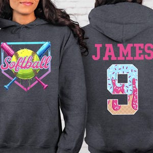 May include: A dark gray hooded sweatshirt with a softball graphic and the word "Softball" in a colorful font. The back of the sweatshirt has the name "JAMES" and the number "9" in a pink and blue ice cream cone design.