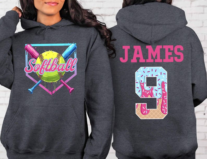 May include: A dark gray hooded sweatshirt with a softball graphic and the word "Softball" in a colorful font. The back of the sweatshirt has the name "JAMES" and the number "9" in a pink and blue ice cream cone design.