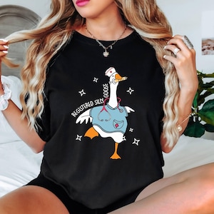 K&ouml;nnte beinhalten: Schwarzes T-Shirt mit einer Cartoon-Gans, die eine Krankenschwesterm&uuml;tze und einen Kittel tr&auml;gt. Der Text "Registered Silly Goose" ist auf dem Shirt aufgedruckt.