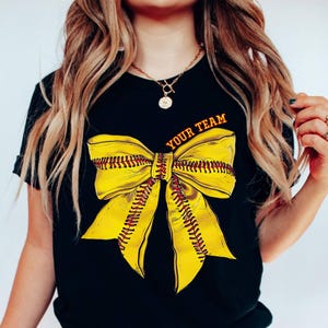 May include: Black t-shirt with a yellow and red softball bow and the text "Your Team" printed on the front.