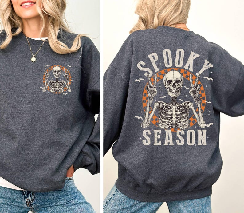 Puede incluir: Una sudadera gris oscura con un gr&aacute;fico de esqueleto y el texto "Spooky Season" impreso en la espalda. El esqueleto est&aacute; levantando dos signos de paz.