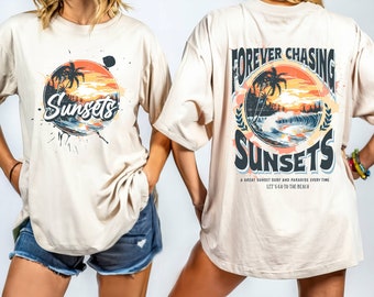 May include: A beige t-shirt with a graphic print of a sunset and palm trees. The text "Forever Chasing Sunsets" is printed on the back of the shirt. The text "A great sunset surf and paradise every time. Let's go to the beach" is printed below the graphic.