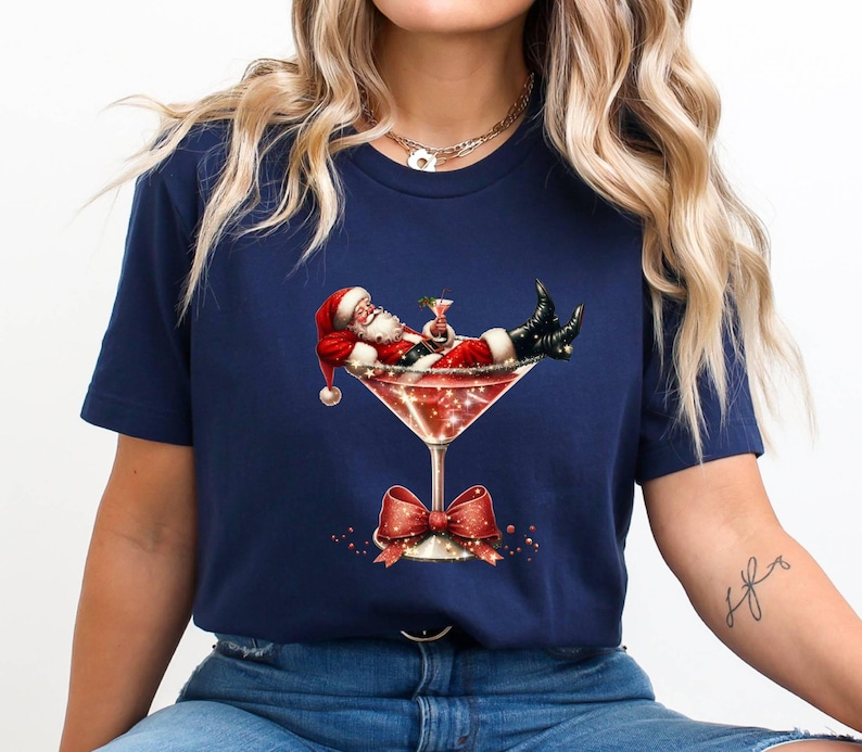 May include: A navy blue t-shirt with a graphic of Santa Claus relaxing in a martini glass with a red bow.