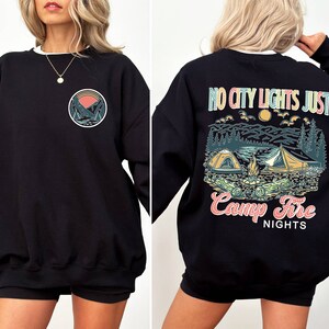 May include: Black sweatshirt with a graphic print of a mountain scene and the text "No city lights just camp fire nights" on the back. The front of the sweatshirt has a smaller graphic of a mountain scene.