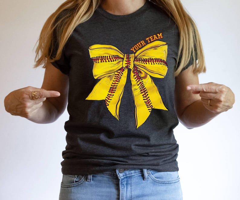 May include: A dark grey t-shirt with a yellow softball bow and the text "YOUR TEAM" printed on the front.