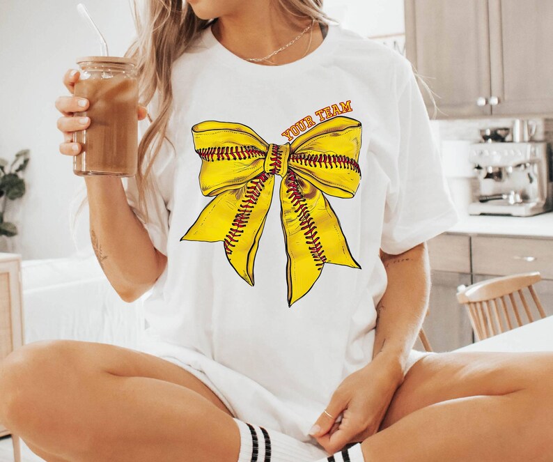 May include: White t-shirt with a yellow softball bow and the text "Your Team" printed on the front.