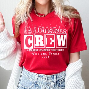 May include: A red t-shirt with the words "Christmas Crew" in white block letters. The shirt also features the text "Making Memories Together" and "Williams Family 2025". Festive Christmas tree and snowflake graphics are also included.