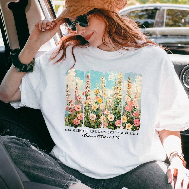 May include: White t-shirt featuring a floral design with pink, yellow, and white flowers against a blue sky background. The text "HIS MERCIES ARE NEW EVERY MORNING Lamentations 3:23" is printed below the floral design.