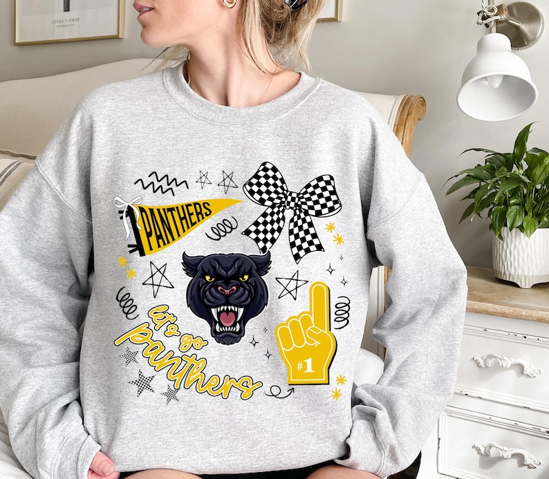 May include: A light gray sweatshirt featuring a black panther graphic with the text "Let's go Panthers." The design includes a checkered bow, a foam finger, stars, and a pennant. The sweatshirt is a comfortable, casual style.
