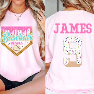 May include: Pink baseball t-shirt with a baseball diamond graphic and the text "Baseball Mama". The back of the shirt has the name "JAMES" and the number "9" with a sprinkle-covered ice cream cone design.