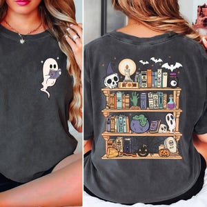 May include: A black t-shirt with a graphic of a ghost reading a book on the front and a bookshelf with spooky Halloween items on the back.