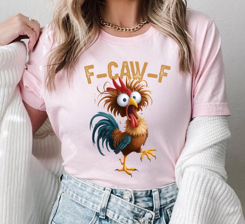 May include: Pink t-shirt featuring a cartoon rooster with wide eyes and an open beak, with the text "F-CAW-F" in gold letters. The rooster has red, brown, blue, and yellow coloring.