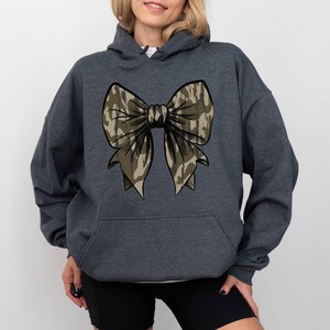 May include: A dark gray hooded sweatshirt with a camouflage bow design on the front.