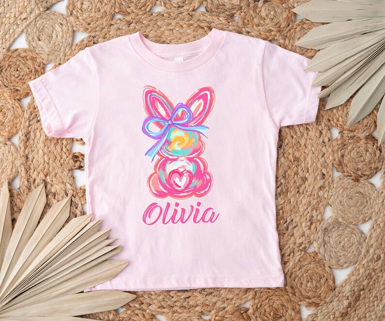 May include: Pink t-shirt with a colorful abstract bunny design and the name "Olivia" printed below.