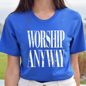 May include: A royal blue t-shirt with the words "WORSHIP ANYWAY" printed in large, distressed white letters. The shirt has a crew neck and short sleeves.