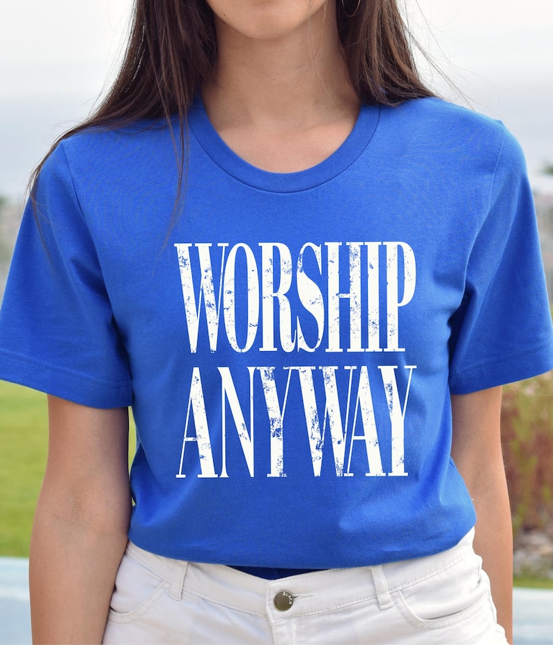 May include: A royal blue t-shirt with the words "WORSHIP ANYWAY" printed in large, distressed white letters. The shirt has a crew neck and short sleeves.