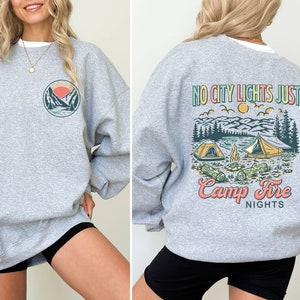 May include: Gray sweatshirt with a graphic of mountains and a sunset on the left side and a graphic of a campfire scene with the text "No City Lights Just Camp Fire Nights" on the right side.