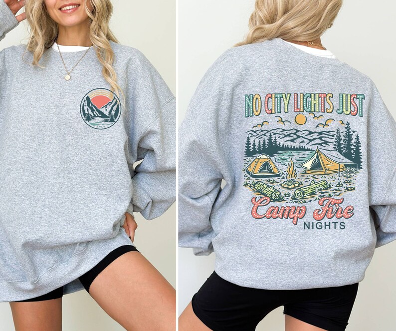 May include: Gray sweatshirt with a graphic of mountains and a sunset on the left side and a graphic of a campfire scene with the text "No City Lights Just Camp Fire Nights" on the right side.